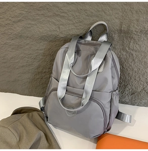 Detailansicht eines grauen Nylon-Rucksacks mit breiten Griffen vor einer strukturierten Wand