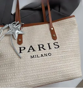 Detail of straw tote bag with Paris Milano embroidery and brown leather handles