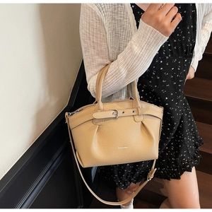 Chic beige pleated handbag with leather buckle detail and adjustable strap on a model