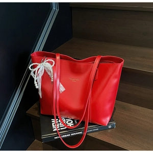 Detailed macro view of a red leather tote bag with elegant pearl lace bow accessory