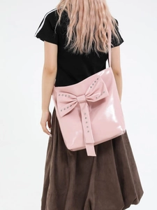 Rosafarbene Handtasche aus Lackleder mit Nietenschleife getragen von einem Model vor Weiß