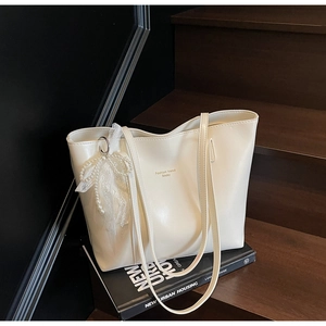Detail of off-white PU leather tote bag with lace bow charm on dark wood stairs