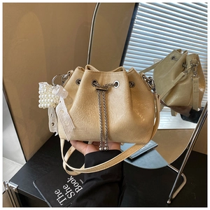 Detail of cream drawstring bucket bag with shiny texture and pearl lace heart charm