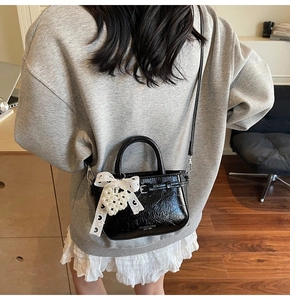 Détail du sac en cuir verni noir avec nœud en dentelle et pendentif perle sur modèle