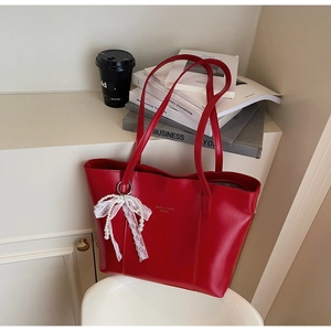 Detail of red faux leather tote bag featuring a white lace and pearl bow charm