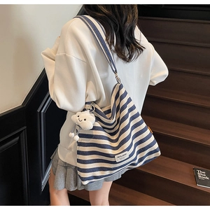 Detail of blue striped canvas tote bag with plush cloud charm on a wooden staircase
