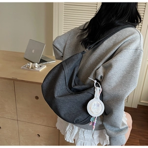 Detail of dark gray crescent crossbody bag with white pendant in a home office scene