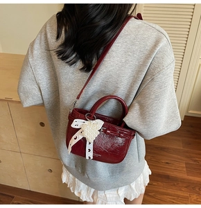 Détail du sac à main rouge foncé en cuir craquelé avec nœud en dentelle et pendentif