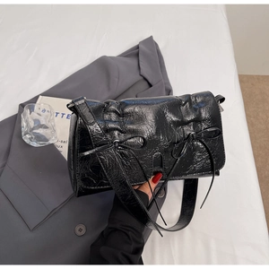 Détail d'un sac à bandoulière en cuir verni froissé noir avec un nœud décoratif élégant