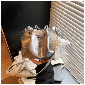 Detail of silver metallic bucket bag with drawstring chain, pearl heart and lace bow