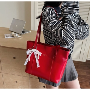 Detail view of red leather tote bag with elegant lace bow pendant and gold lettering