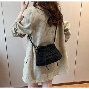 Detail einer schwarzen Leder-Umhängetasche mit Schleife auf einem beigen Blazer-Outfit