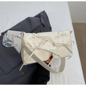 Détail du sac à bandoulière crème en cuir verni brillant avec nœuds et boucles argentées