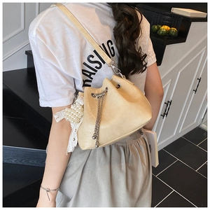 Detail of beige glossy bucket bag featuring metal chain drawstring and pearl lace charm