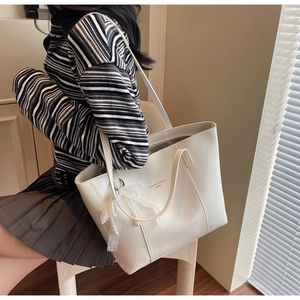 Detail of white tote bag with elegant pearl lace bow charm and printed logo text