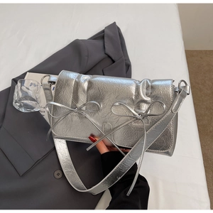 Sac à main argenté métallisé avec texture plissée et deux nœuds posé sur un blazer