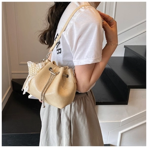 Detail of beige drawstring bucket bag with pearl lace bow charm and silver chain strap