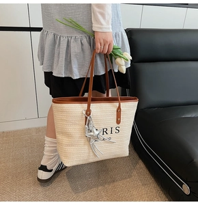 Detail of woven beige tote bag with brown leather straps and star pendant accessory