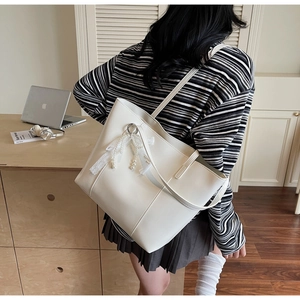 Detail of white leather tote bag featuring lace pearl bow charm and minimalist stitching