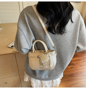 Detail view of cream white tote bag with pearl pendant and lace bow on a model