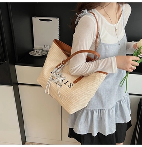 Detail of beige straw tote bag with leather handles and Paris Milano printed text