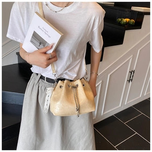Detail of creamy yellow drawstring bucket bag with glossy pleated leather and silver chain
