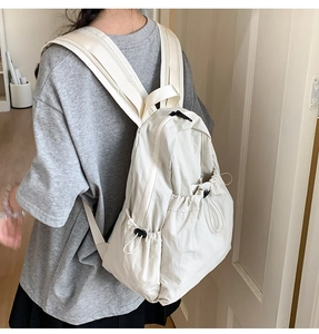 Detail view of cream drawstring nylon backpack showing side pocket and thick shoulder straps
