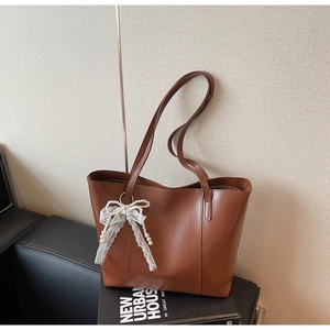 Detail of vintage brown tote bag featuring lace bow and pearl pendant on leather sofa