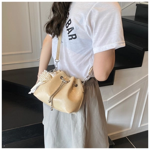 Close-up of beige drawstring bucket bag featuring a large pearl cluster and chain