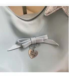 Close-up of light blue shoulder bag featuring a leather bow and engraved heart pendant