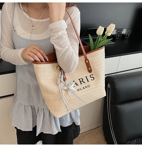 Detail of a beige woven tote bag with brown leather handles and star charm accessory