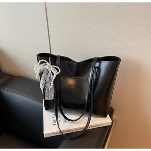 Detail of black faux leather tote bag featuring a lace pearl bow and fashion logo