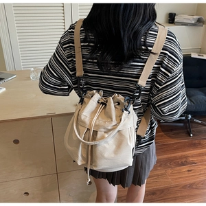 Detail of beige drawstring bucket bag featuring adjustable nylon straps in a lifestyle setting