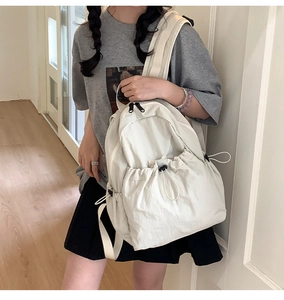 Detail of cream drawstring backpack showing crinkled nylon texture and black zipper accent