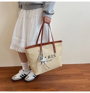 Detail of woven straw tote bag featuring leather handles and star fringe charm