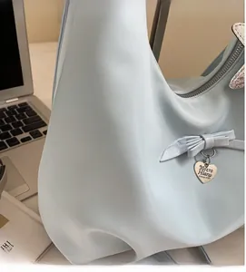 Detail of light blue hobo bag showing soft silk texture, ribbon knot, and heart pendant
