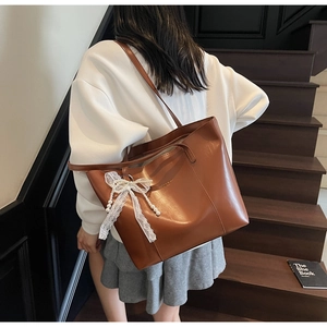 Brown leather tote bag featuring a decorative lace pearl bow pendant on the side