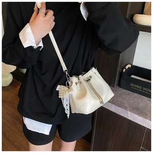 Detail of white PU bucket bag featuring a pearl lace charm and metallic drawstring chain