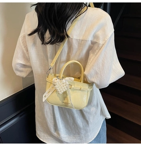 Close-up of yellow patent leather handbag with lace bow and pearl heart charm detail