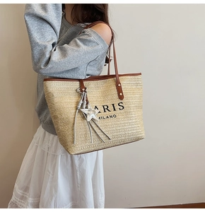 Detail of woven straw tote bag with brown straps and star tassel charm on shoulder