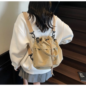 Detail of beige drawstring bucket bag with black metal hooks on wooden stairs