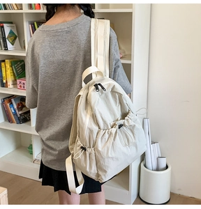 Detail of cream drawstring backpack showing side pocket and textured fabric on model