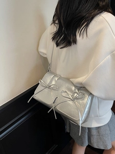 Sac à main argenté avec nœud et texture plissée porté à l'épaule vue de trois quarts