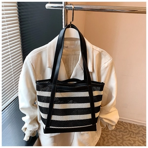 Detail view of large striped mesh tote bag with black leather handles for summer use