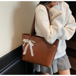 Detail of a brown leather tote bag with lace and pearl bow charm on a model's shoulder