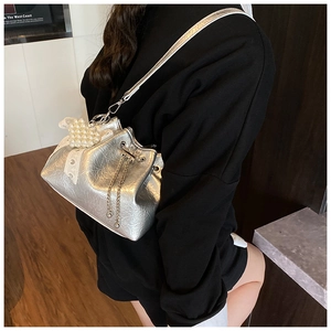 Detail of silver metallic drawstring bucket bag with pearl heart charm and metal chain
