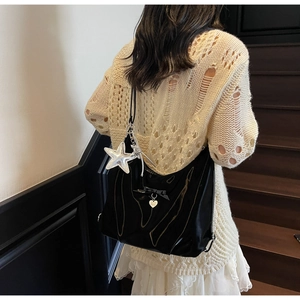 Close-up of black patent leather hobo bag with bow, gold heart charm and silver star