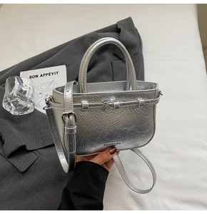 Détail d'un sac à main argenté plissé en cuir souple posé sur une veste de costume