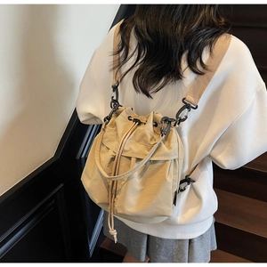 Detail view of a beige drawstring bucket backpack featuring versatile black shoulder straps