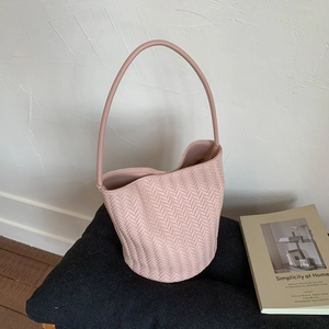 Detail shot of pink woven bucket bag with intricate V-pattern texture on grey cushion